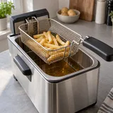 Een kleine portie goudgele friet in het mandje boven een elektrische frituurpan.