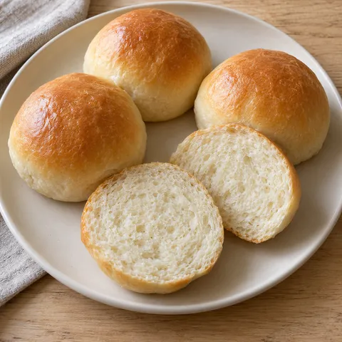 Zachte witte bolletjes met lichtgouden korst en een doorgesneden broodje met fijne kruim