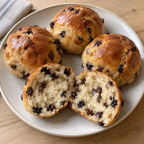 Goudbruine krentenbollen met een opengesneden bol vol donkere krenten